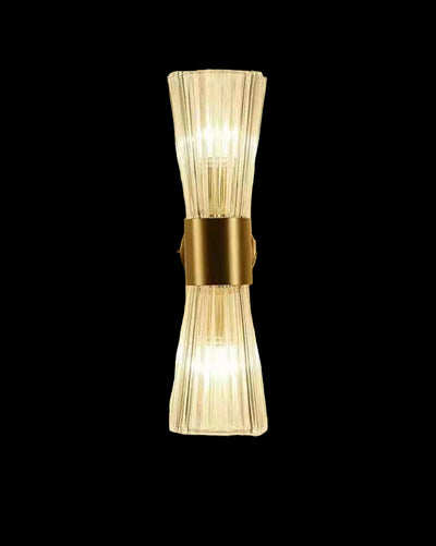 Wall-mounted light fixture with clear glass shade and gold metal base on a beige wall.